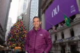 Imagem mostra jovem executivo de casado com árvore de Natal e logo do Nubank atrás.