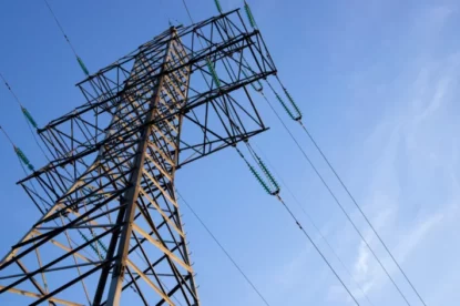 Imagem mostra torre de transmissão de energia sob céu azul.