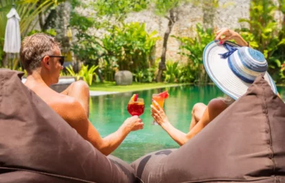 Casal brinda com seus drinks sentados à beira de uma piscina no resort.