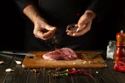 Chef polvilha especiarias em bife de carne para cozinhar no almoço de churrasco. Imagem remete ao boicote de frigoríficos contra a rede varegista Carrefour (CRFB3) no Brasil.