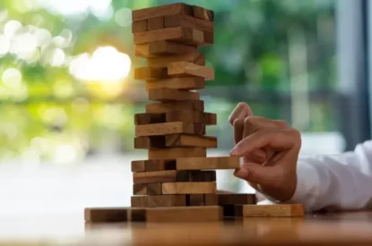 Mão de garota tenta arrancar bloco de madeira sem derrubar a torre de Jenga. Conceito de risco de negócios.