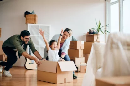 Pais e criança brincam em meio a caixas durante mudança para uma nova casa.