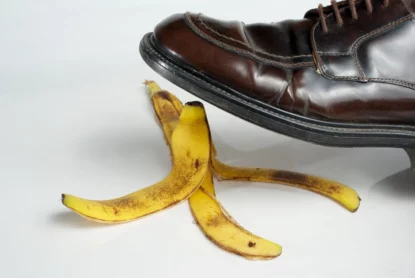 Imagem mostra detalhe de sapato a ponto de pisar em casca de banana. Conceito de cilada, maus negócios, compra de imóvel furada.