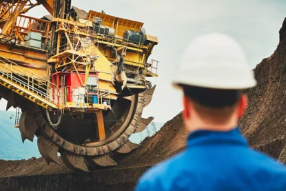 Máquina de mineração trabalha em extração a céu aberto observada por funcionário de capacete.