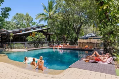 Imagem mostra hóspedes em piscina de hotel, rodeada de árvores, em um lindo dia de sol.