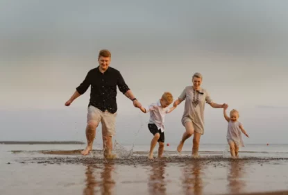 Imagem mostra família de pais com dois filhos brincando na praia.