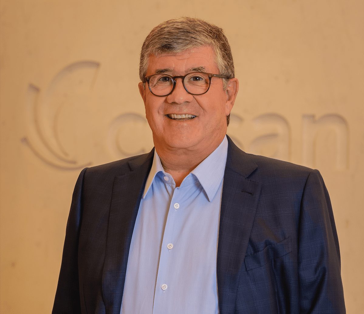 Retrato de homem sorrindo, de óculos e camisa azul, com logo da Cosan em relevo ao fundo.