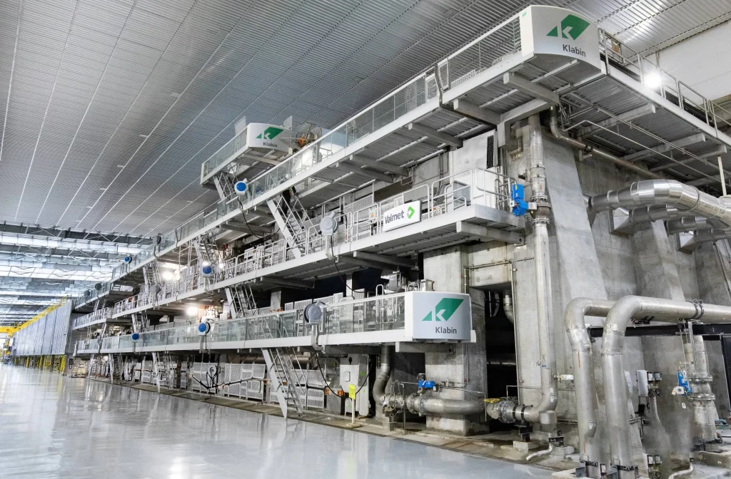 Complexa máquina de produção Klabin/Valmet domina o interior de uma fábrica industrial espaçosa e moderna.