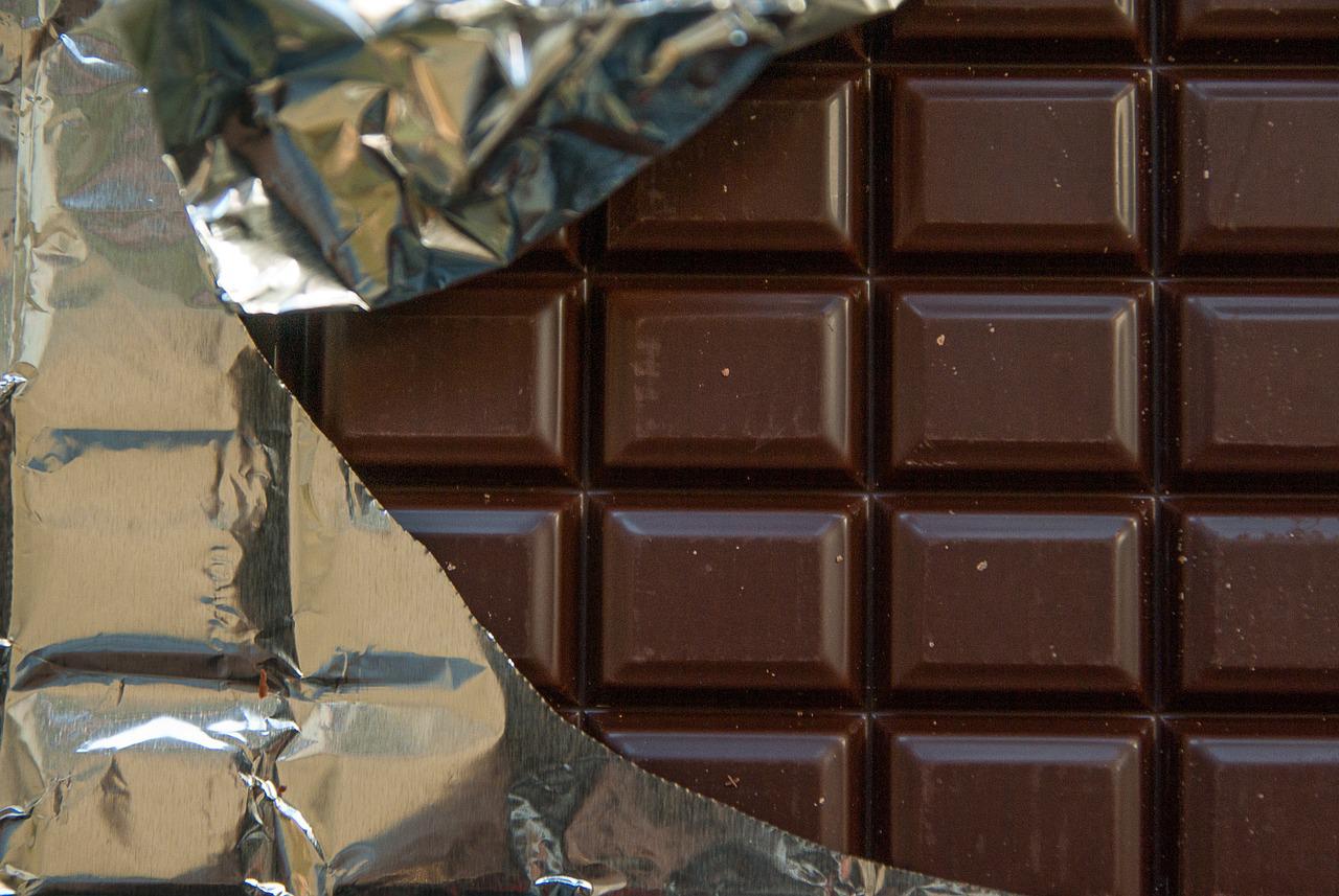 Barra de chocolate escura com embalagem de alumínio aberta, exibindo seus quadrados.
