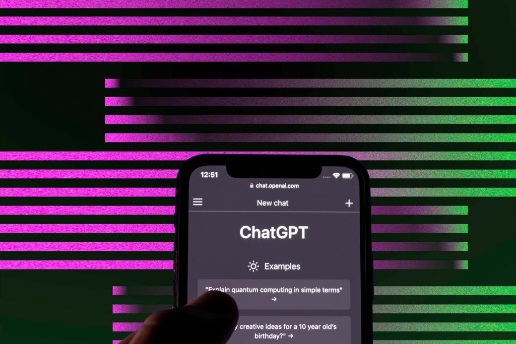 Smartphone com ChatGPT exibido em tela escura, segurado por uma mão, em fundo digital de barras rosa e verde.